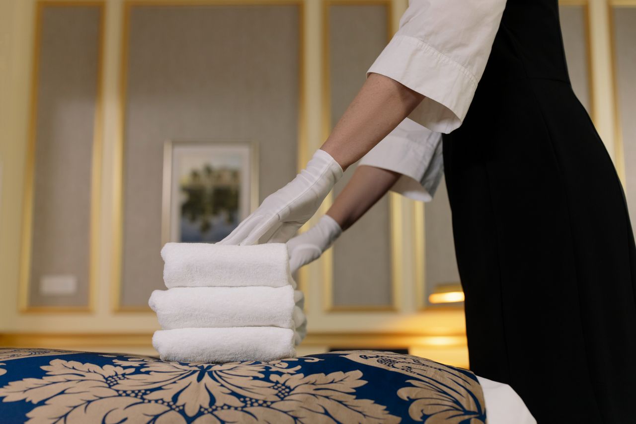 A hotel housekeeper neatly stacks fresh towels in a luxurious room setting.